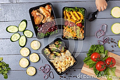 Food container boxes and girl hand holds spoon, raw vegetables, zuchini and eggplants, carrot and onion, place for text in center Stock Photo