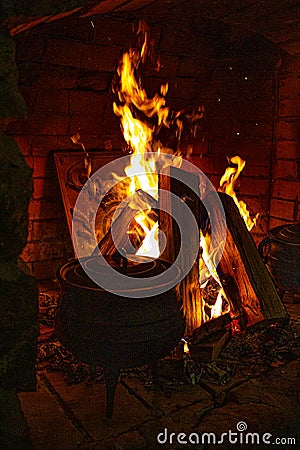 Food is cooked in the fireplace. Spread the fire. Bonfire and firewood. Fire. Cast iron casserole in the oven. Logs in Stock Photo