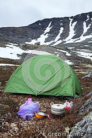 Food cooking on portable gas stove during hiking, green tent is on mountain valley for sleeping, mountains with severe weather and Stock Photo