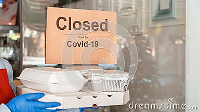 Food for delivery against sign closed due to covid 19. Waiter in gloves work with takeaway orders. Waiter giving takeout meal Stock Photo