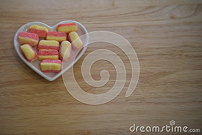 Food photography of sugar candy sweets flavored with rhubarb and custard in pink and yellow colors in a white love heart dish Stock Photo