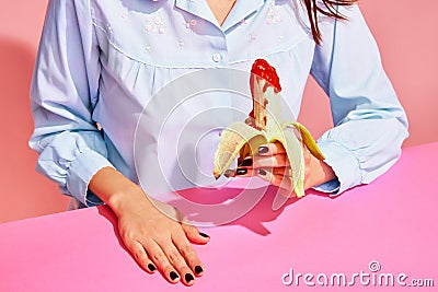 Food pop art photography. Young woman tasting banana with tomato ketchup isolated on pink background. Vintage, retro Stock Photo