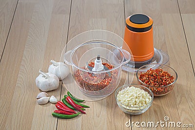 Food processor with chopped chilli and garlic on wooden table Stock Photo