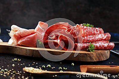 Food tray with delicious salami, coppa, crudo and herbs. Meat platter with selection on rustic table Stock Photo