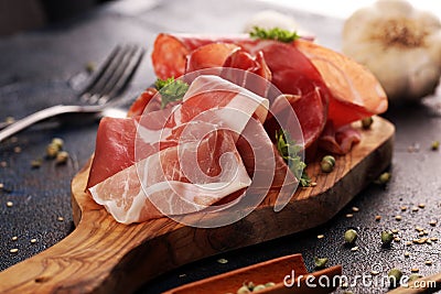 Food tray with delicious salami, coppa, crudo and herbs. Meat platter with selection on rustic table Stock Photo