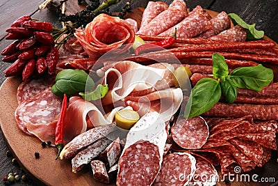 Food tray with delicious salami, pieces of sliced prosciutto crudo, sausage and basil. Meat platter with selection Stock Photo