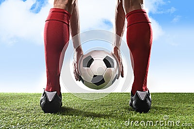 Football player in red socks and black shoes holding ball in his hands placing free kick or penalty Stock Photo