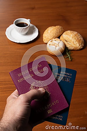 In the foreground, Italian and Brazilian passport, in the background and blurred a small cup of coffee and three loaves of bread w Stock Photo