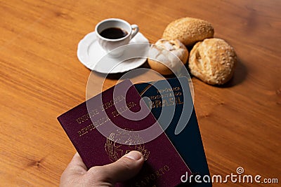 In the foreground, Italian and Brazilian passport, in the background and blurred a small cup of coffee and three loaves of bread w Stock Photo
