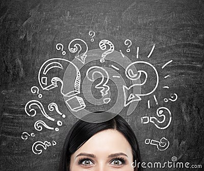 A forehead of the girl who is pondering about unsolved problems. Question marks are drawn around the head. black chalkboa Stock Photo