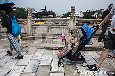 A foreign girl sitting in a stroller holding a toy and passing by on the Wende Bridge Editorial Stock Photo