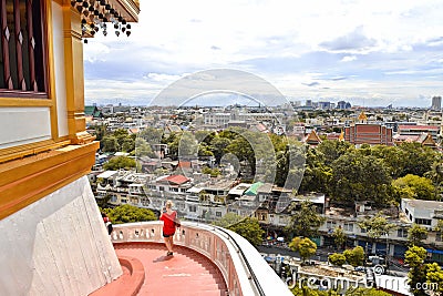 Foreign tourist with red dress descends the stairs of the temple of the golden mount with city scape in background in Bangkok Thai Editorial Stock Photo