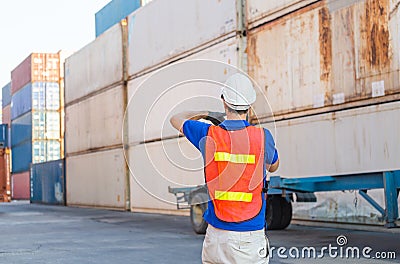 Foreman worker in hard hat and safety vest talks on two-way radio control loading containers box from cargo Stock Photo