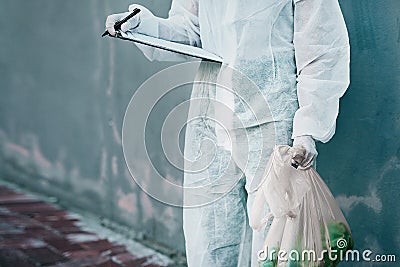 Forensic investigator collecting evidence on a murder scene on a street holding a plastic bag and wearing a hazmat suit Stock Photo