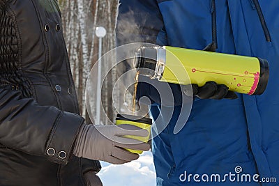 In the forest, in the cold, a man pours a woman hot tea from a thermos Stock Photo