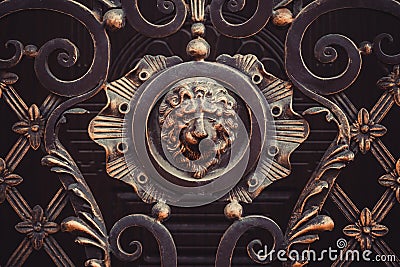 Forged ornate gate details with lion head cast iron sculpture, bronze colored, rosette style. Metal products, ironwork. Gates Stock Photo