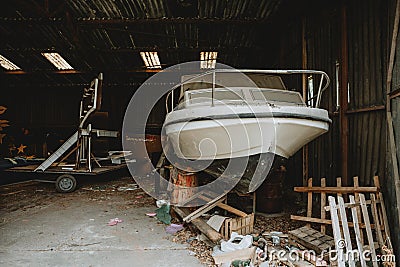 Forgotten abandoned old boat covered with layer of dust hidden in old barn full of mess and other old things Stock Photo