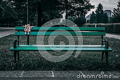 Forgotten children`s toy on a lonely green, park bench Editorial Stock Photo