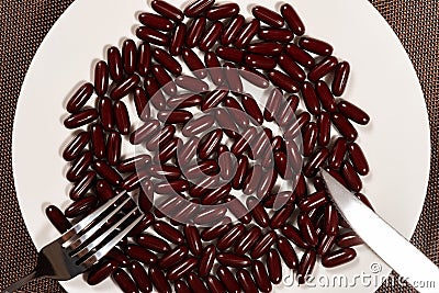 Fork and knife with lots of capsules on dish concept of over-relying on medicine Stock Photo