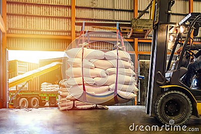 Forklift handling white sugar bags for stuffing into containers outside a warehouse. Stock Photo