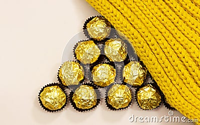 Forming triangle shape from golden premium chocolate sweets under woolen winter scarf Stock Photo