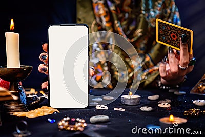 The fortune teller is holding a Tarot card and a smartphone with a white screen. Mock up. Close-up. The concept of divination, Stock Photo