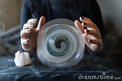 Fortune teller holds hands above magic crystal ball with eyeball inside. Conceptual image of black magic and occultism Stock Photo