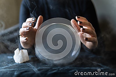 Fortune teller holds hands above magic crystal ball with smoke around. Conceptual image of black magic and occultism Stock Photo