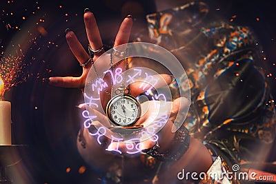 The fortune teller holds a watch on a chain in her hands and conjures over it. A luminous zodiac circle is depicted around the Stock Photo