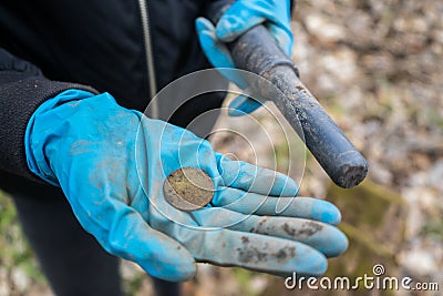 Found old precious coin in archaeologist hand with pinpointer metal detector. Stock Photo