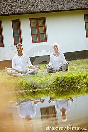 They found a tranquil spot to meditate together. Full length shot of a mature couple meditating beside a pond. Stock Photo