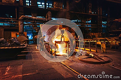 Foundry workshop interior, molten iron pouring from blast furnace into ladle container and workers founders control Stock Photo