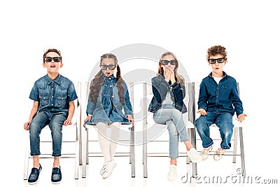 Four amazed kids in 3d glasses sitting on chairs on white. Stock Photo