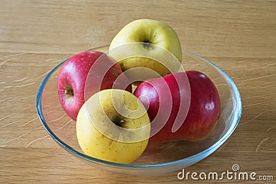 Four apples, two yellow and two red, in a glass bowl on a wooden table Stock Photo