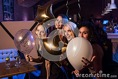 Four beautiful young Caucasian women holding balloons having night out together in trendy bar Stock Photo