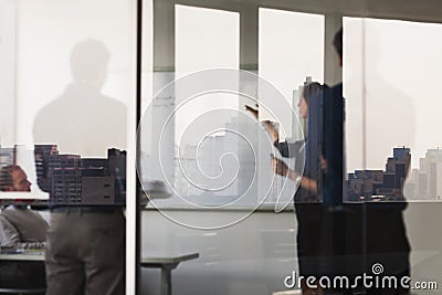Four business people standing and looking at a white board on the other side of a glass wall Stock Photo
