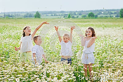 Four children in a flowery chamomile meadow. Friends are having fun in a field of daisies. Boys and girls wave their hands and Stock Photo