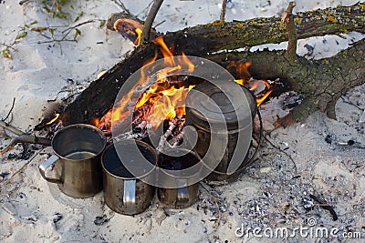 The four cups and kettle heats water on the fire. Camping beach, summer time, fireplace Stock Photo