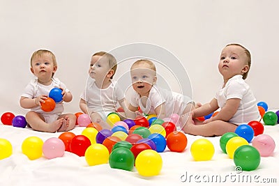 Four cute funny babies sitting on the white blanket and playing colorful balls. Infant party. Stock Photo