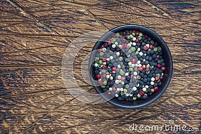 Four different kinds of peppercorns in clay bowl on wooden background, copy space, top view Stock Photo