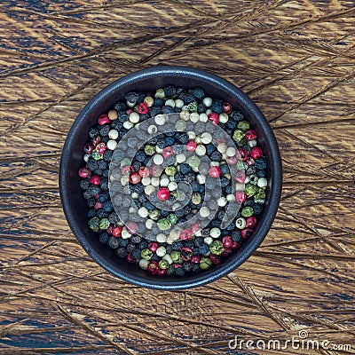 Four different kinds of peppercorns in clay bowl on wooden background, square format, top view Stock Photo