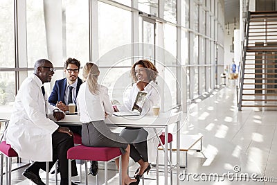 Four doctors talking at a table in a modern hospital lobby Stock Photo