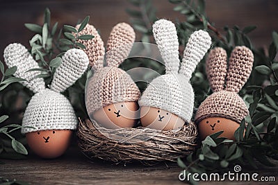 Four Easter eggs in crochet hats with rabbit ears in a nest on a wooden table. Stock Photo