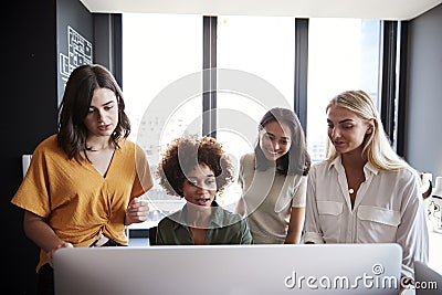 Four female creatives working around a computer monitor in an office, front view, close up Stock Photo