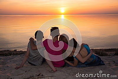 Four friends hugging on the beach and admiring the sunset Stock Photo