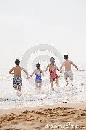 Four friends running into the water on a sandy beach, rear view Stock Photo