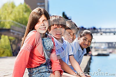 Four friends sitting in a line on bank of river Stock Photo