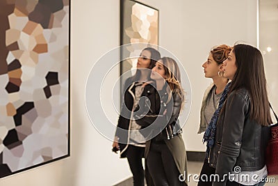 Four girl friends looking at modern painting in art gallery Stock Photo