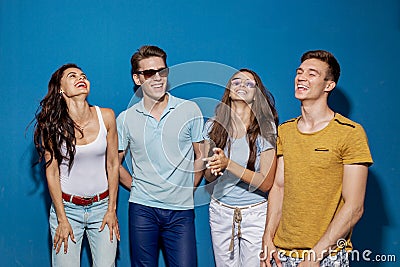 Four good-looking friends are laughing while standing in front of the blue wall. Entertainment, having good time Stock Photo