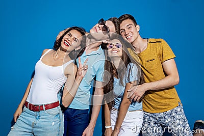 Four good-looking friends are laughing while standing in front of the blue wall having confident and happy looks Stock Photo